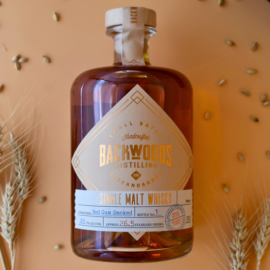 Backwoods Distilling single malt whisky bottle with a decorative label on an orange background.