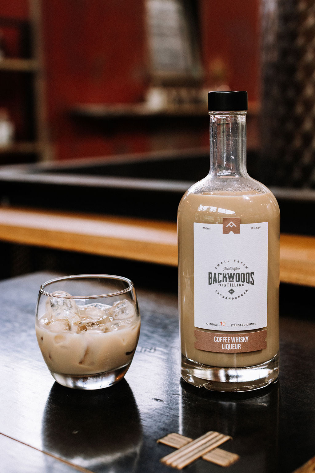 Bottle of Backwoods Coffee Whisky Liqueur with a glass of the drink on a bar counter.