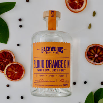 Bottle of Backwoods Distilling Co. Blood Orange Gin with a label on a white background with blood orange slices and spices.