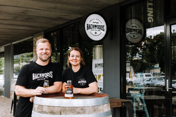 Leigh and Bree Attwood standing behind a barrel at the front of Backwoods Distilling Co's distillery door in Yackandandah.