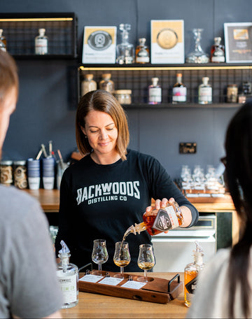 Bree pouring a tasting paddle with shelves of bottles in the background